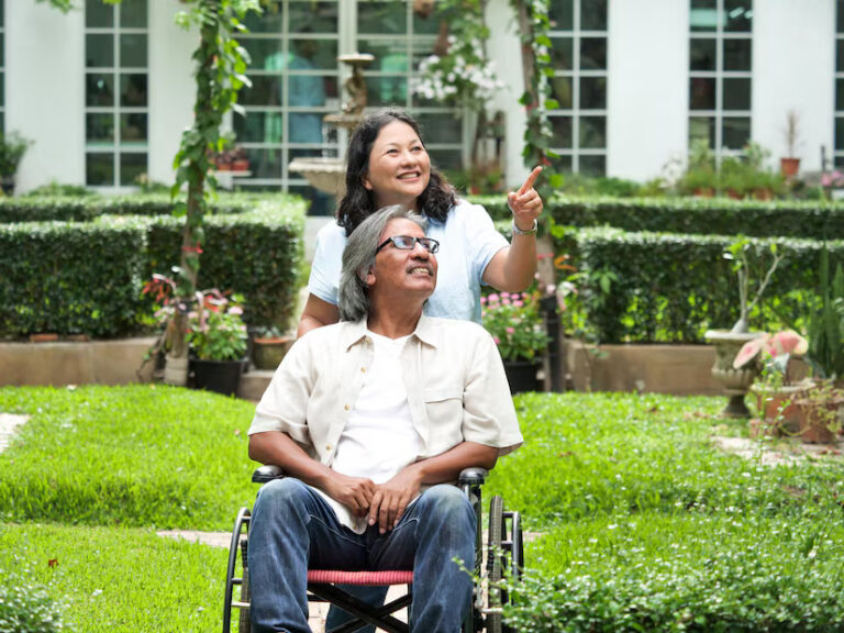 smiling-woman-pointing-while-man-sitting-wheelchair-yard_1048944-15656593